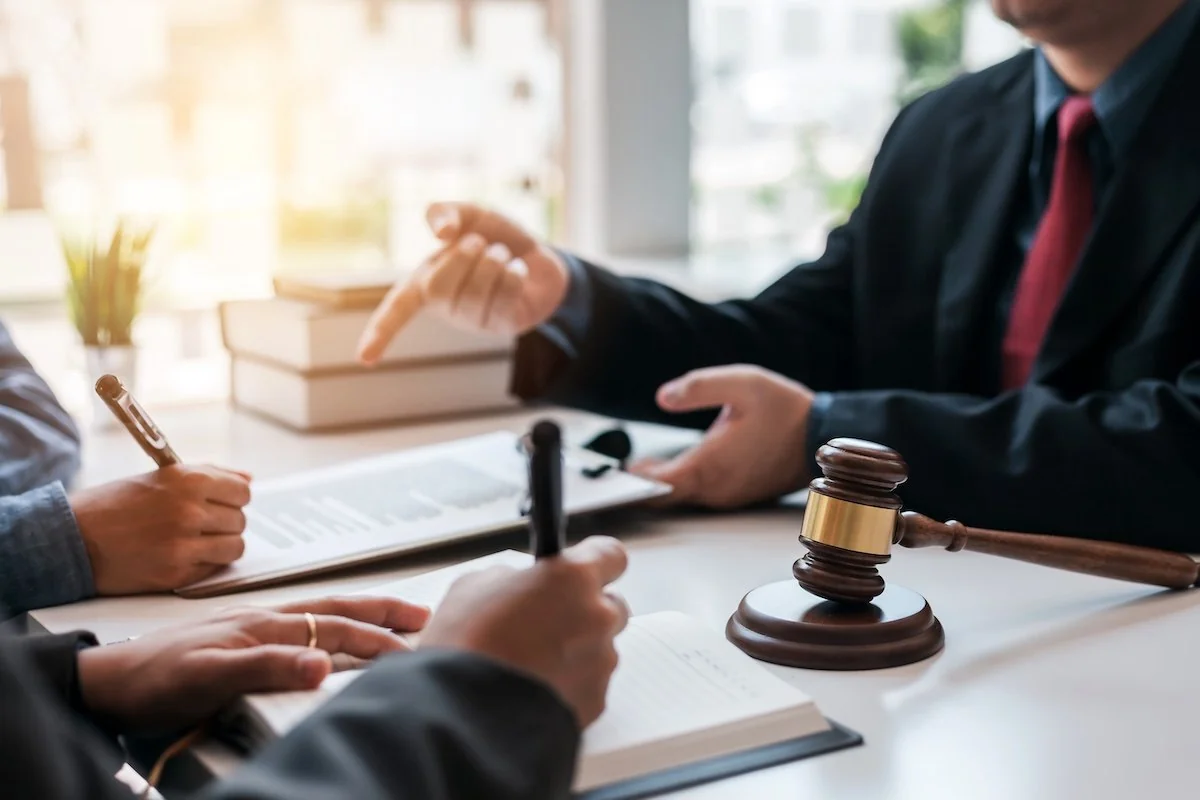 An attorney in a suit discussing documents with clients across a desk, a gavel in the foreground