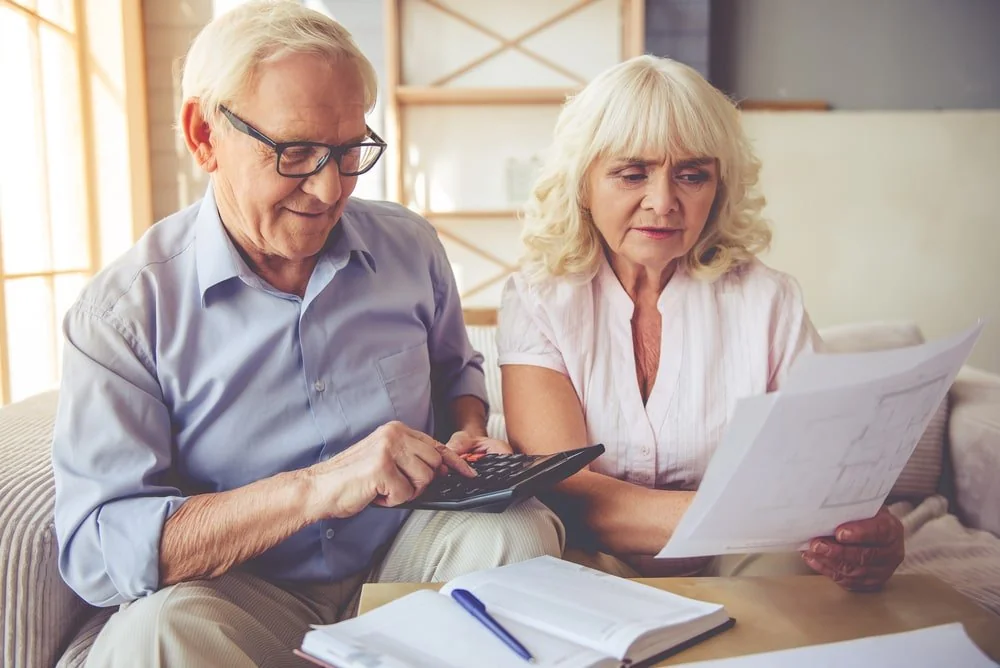 A senior couple reviewing household paperwork and a calculator together at home