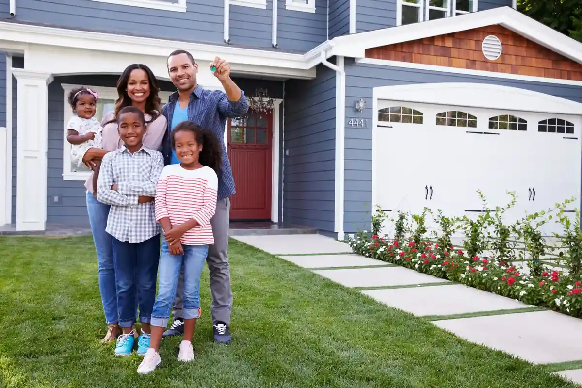 A family holding the keys to their new home, standing on the lawn in front of it